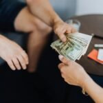 Close-up of hands exchanging US dollar bills, symbolizing a financial transaction or payment.