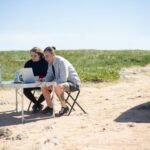 Two adults working on laptops outdoors in Portugal, enjoying a sunny day with portable workspace.